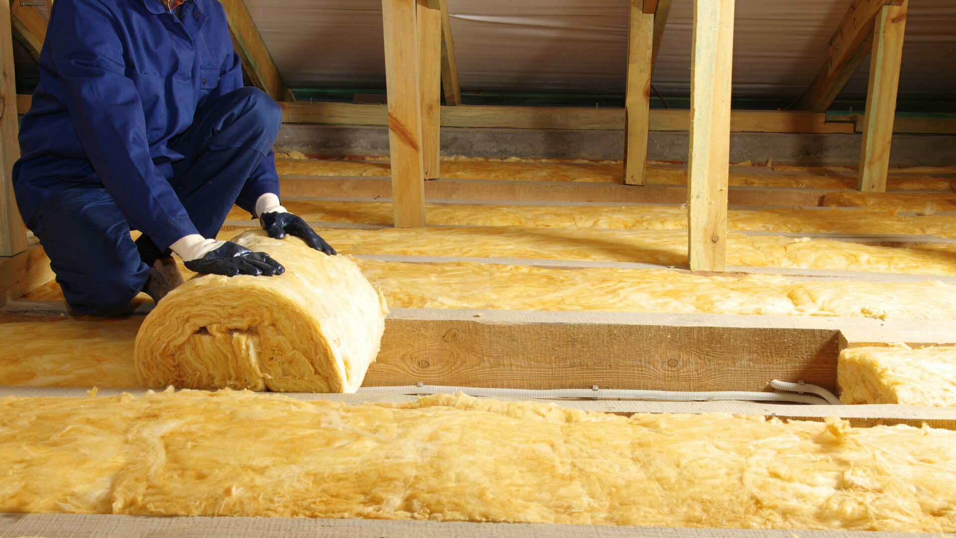 Construction worker thermally insulating house attic with glass wool